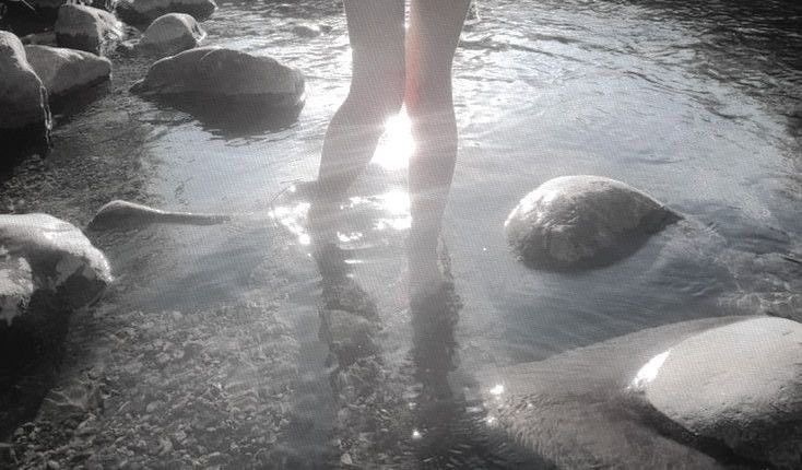 girl with feet waiding in ocean water, sun is shining on the water, girl is pale and the water is deep duskey blue